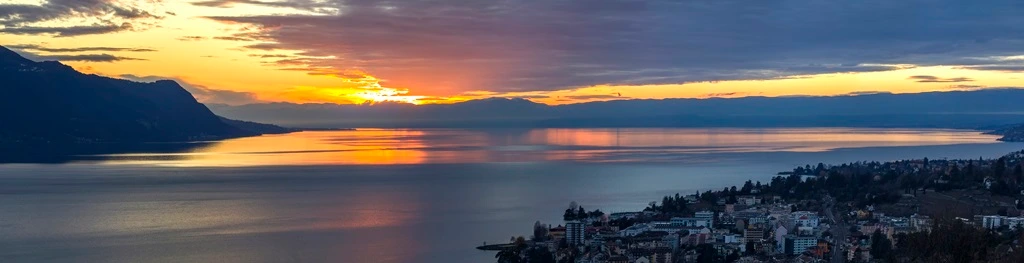 Vista panorámica de la puesta de sol sobre el lago Leman con cielo amarillo con nubes y montañas de los Alpes
