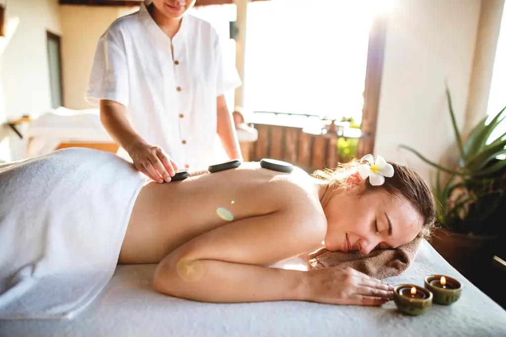Mujer recibiendo un masaje con piedras calientes mientras escucha música zen