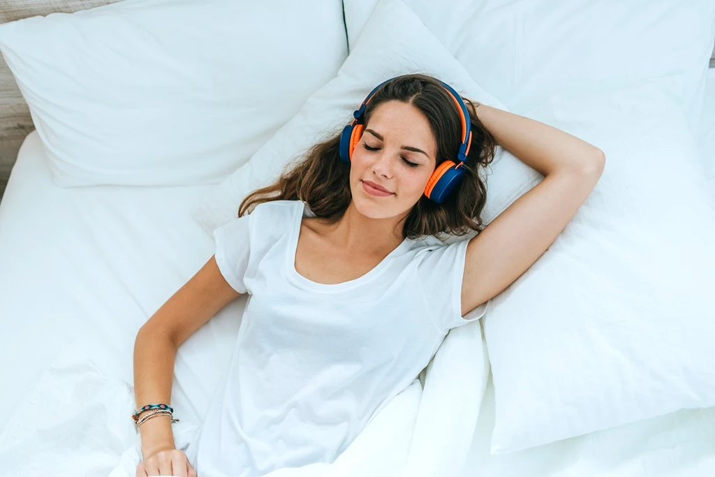 Mujer joven relajada en la cama escuchando música zen con auriculares
